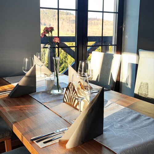 Stół w restauracji z widokiem na górski krajobraz, elegancko ustawiony z serwetkami, kieliszkami i kwiatami w wazonie