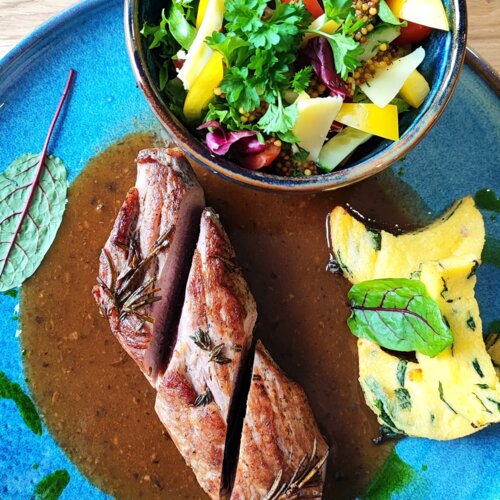 Stek podany z sosem, ziemniakami i świeżą sałatką z warzyw w ceramicznej misce