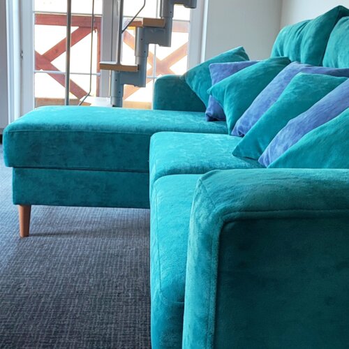 Wygodna turkusowa sofa z poduszkami w nowoczesnym wnętrzu z widokiem na balkon i schody do sypialni