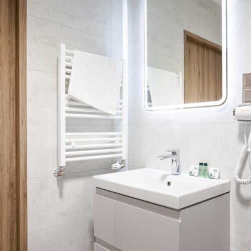 Nowoczesna łazienka hotelowa z podświetlanym lustrem, umywalką, suszarką do włosów i białym grzejnikiem na ręczniki