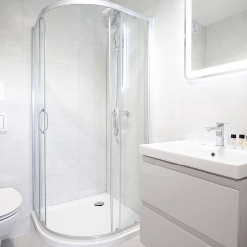 Nowoczesna łazienka w hotelu z prysznicem z przezroczystymi drzwiami, umywalką z kosmetykami i podświetlanym lustrem