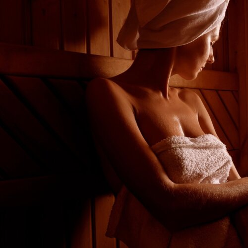 Zrelaksowana kobieta owinięta ręcznikiem siedzi w drewnianej saunie o przytulnej atmosferze spa