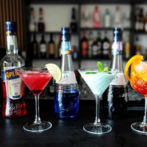 Kolorowe koktajle z lodem i świeżymi plasterkami cytrusów ustawione przy barze w nowoczesnym hotelowym salonie barowym