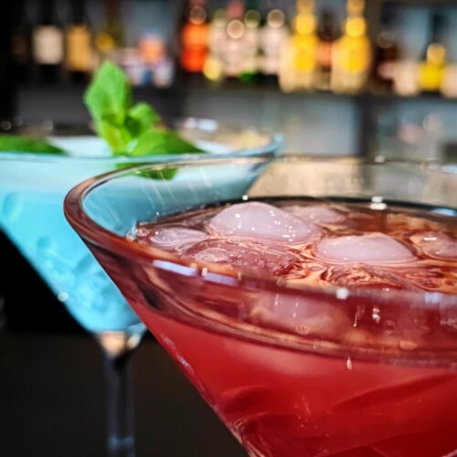 Kolorowe koktajle na lodzie w eleganckich kieliszkach w hotelowym barze z rozmytym tłem alkoholi na półkach