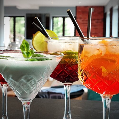 Cztery kolorowe koktajle w eleganckich szklankach z lodem i owocowymi dekoracjami na barze hotelowej restauracji.