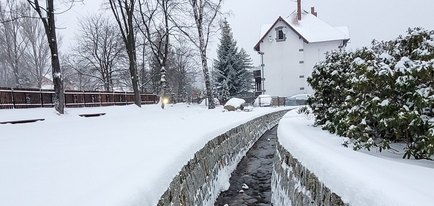 Ruisseau hivernal à Szklarska Poręba avec arbres et pension en arrière-plan.
