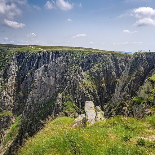 Strome Śnieżne Kotły polodowcowe i zielone łąki w górskim krajobrazie pod jasnoniebieskim niebem.