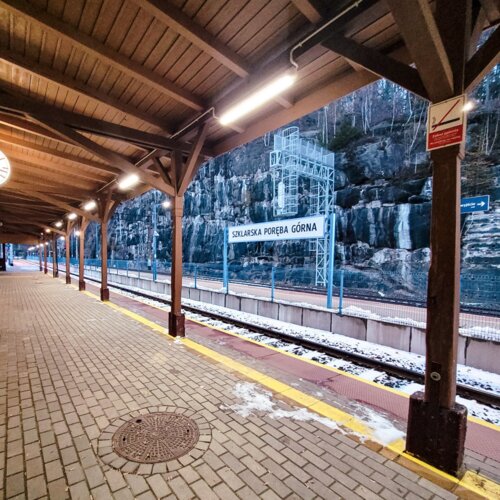 Peron kolejowy Szklarskiej Poręby Górnej z dachem, z widokiem na górskie skały w tle.