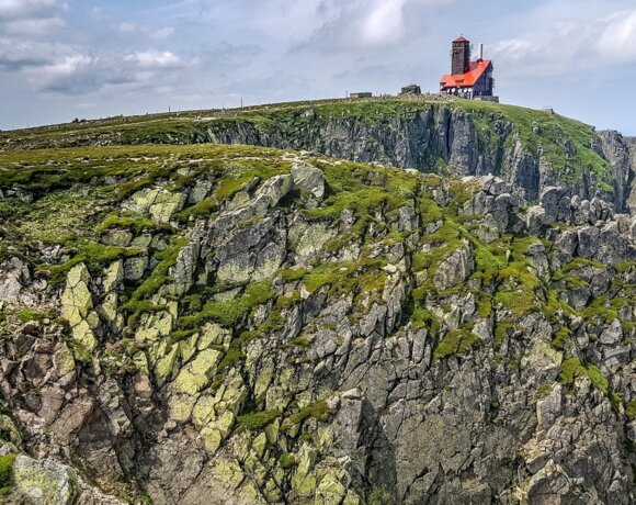 Bâtiment rouge sur une montagne rocheuse avec une végétation verte sous un ciel bleu.