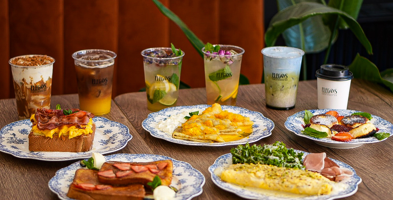 Śniadaniowy zestaw na stole z niebieskimi wzorzystymi talerzami: omlet z zieleniną, tost z bekonem, francuski tost z truskawkami, naleśniki i mrożona kawa.