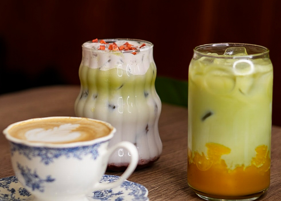 Filiżanka vintage z latte art i dwa warstwowe mrożone napoje matcha — kremowe, owocowe, ozdobione, na drewnianym stoliku