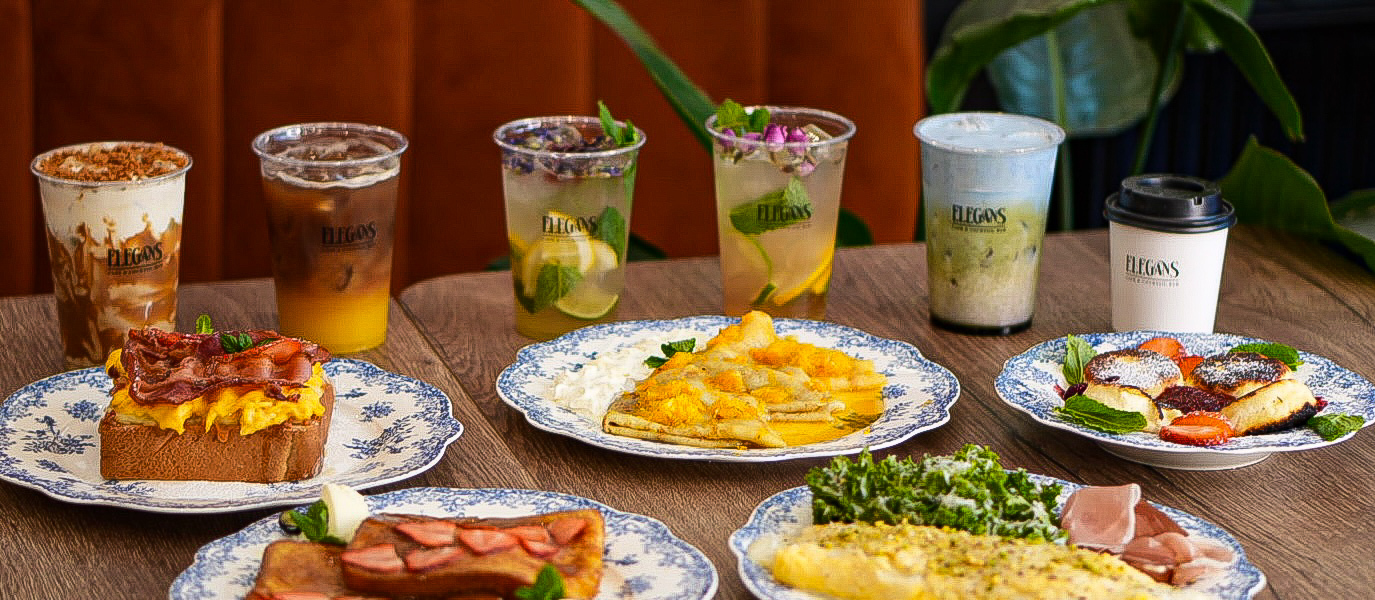 Śniadaniowy zestaw na stole z niebieskimi wzorzystymi talerzami: omlet z zieleniną, tost z bekonem, francuski tost z truskawkami, naleśniki i mrożona kawa.