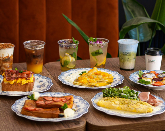 Śniadaniowy zestaw na stole z niebieskimi wzorzystymi talerzami: omlet z zieleniną, tost z bekonem, francuski tost z truskawkami, naleśniki i mrożona kawa.