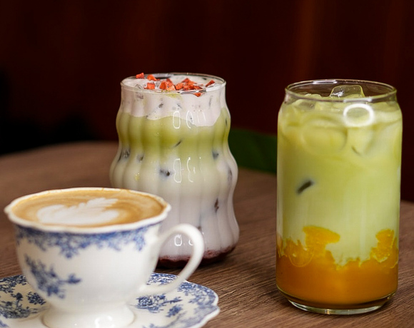 Filiżanka vintage z latte art i dwa warstwowe mrożone napoje matcha — kremowe, owocowe, ozdobione, na drewnianym stoliku