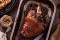 Glazed roasted pork knuckle in a roasting pan with whole-grain mustard and roasted cauliflower on a rustic wooden table
