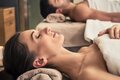 Couple enjoying candlelit spa massage; woman resting on massage table with rolled towel, hand held, soft candlelight