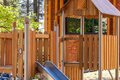 Children's wooden playhouse with slide on hotel grounds beside a red-brick building, shaded by trees.