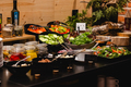 Hotel salad buffet on a cozy wooden counter with sliced cucumber, mixed greens, tomatoes, pickles and dressings