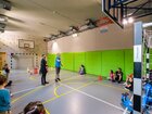 Hala sportowa hotelu z koszem do koszykówki, ścianką wspinaczkową i zielonymi panelami; rodziny i dzieci bawią się.