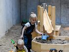 Wewnętrzna piaskownica z drewnianym korytem wodnym, zabawkami i dwójką bawiących się dzieci — rodzinne miejsce zabaw w hotelu.