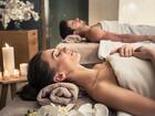 Couple receiving a relaxing couples massage on spa beds with soft towels, lit candles and orchids creating a tranquil ambiance
