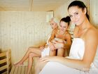 Three women in towels relaxing on wooden benches inside a bright hotel sauna, warm, calm spa atmosphere