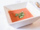 Chilled tomato gazpacho in a square white bowl, garnished with chopped herbs, served on a white tablecloth