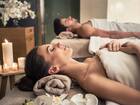 Para relaksuje się podczas masażu dla dwojga na łóżkach spa, w blasku świec, z ręcznikami i orchideami.