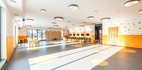 Jasne dziecięce pomieszczenie zabaw w hotelu z pomarańczowymi kropkami, stolikami, pufami, schowkami i dużymi oknami.
