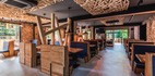 Restauracja hotelowa w stylu rustykalno‑nowoczesnym z drewnianymi boksami, dekoracyjnym sufitem z listew, lampami i oknami z widokiem na las