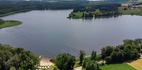 Widok z lotu ptaka na jezioro z hotelową piaszczystą plażą, parasolami, wypożyczalnią łodzi i zalesionym brzegiem