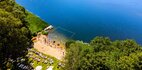 Piaszczysta plaża nad jeziorem z wyznaczonym kąpieliskiem, trawiasty taras z leżakami i parasolami, kajaki i bawiący się goście.