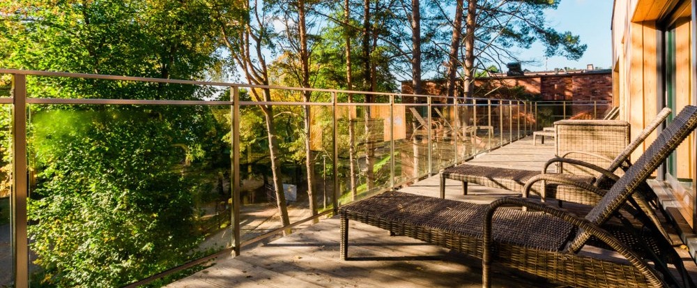 Private wooden balcony with wicker sun loungers, glass railing and treetop forest view, sunny relaxing hotel terrace.