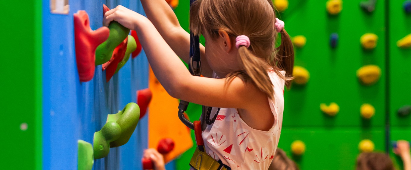 Colorful indoor climbing wall with children in safety harnesses enjoying a supervised kids' activity area