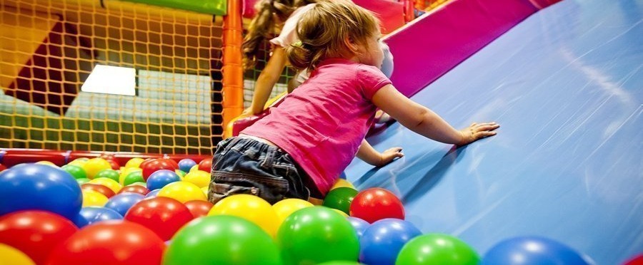 Toddlers climbing a soft blue slide into a colorful ball pit in a hotel's indoor kids' play area