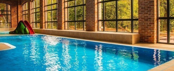 Indoor heated pool with arched brick windows, natural light, bench seating and a small children's slide overlooking trees.