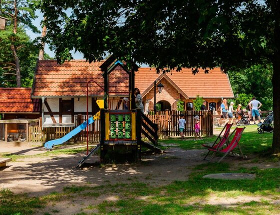 Playground with slide and tic-tac-toe panel, shaded lawn with deck chairs and rustic red-tiled guest cottages nearby