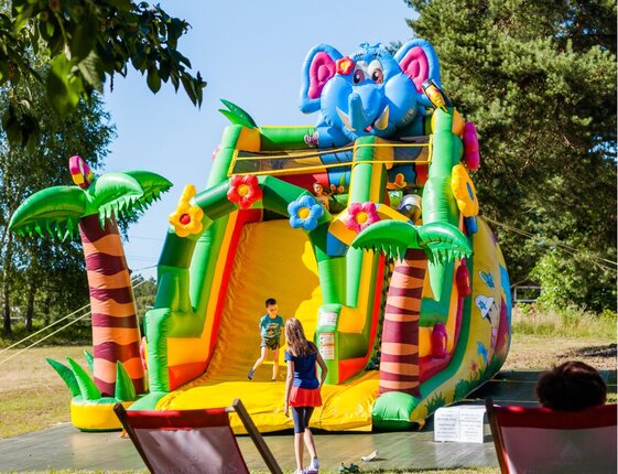 Colorful elephant-themed inflatable slide on a sunny lawn, children playing in a hotel’s outdoor kids' play area.