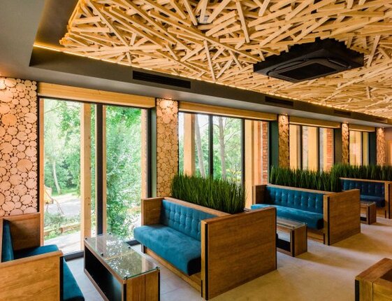 Modern hotel lounge with teal booth seating, wooden-framed tables, floor-to-ceiling windows and decorative wooden ceiling.