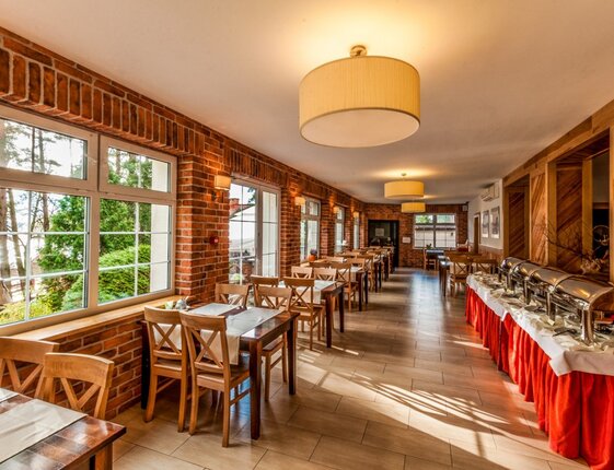 Bright dining room with exposed brick, large windows overlooking trees and water, wooden tables and buffet with chafing dishes.