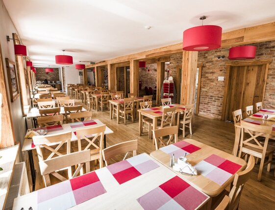 Bright rustic hotel dining room with wooden tables and chairs, red pendant lamps, checkered placemats and exposed brick