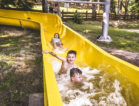 Children splashing down a bright yellow outdoor water slide at a family-friendly resort waterpark