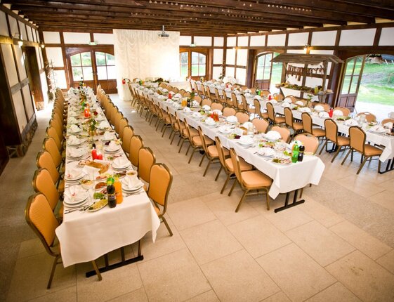 Rustic banquet hall with exposed wooden beams, long white clothed tables set with plates, glassware, salads and drinks.