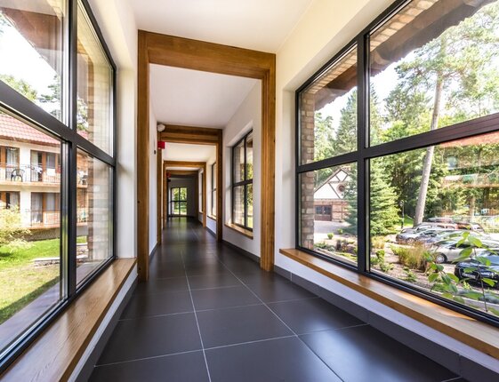 Bright glass corridor with wood frames, tiled floor and panoramic garden and parking views from hotel walkway