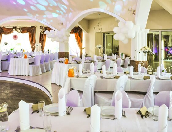 Elegant banquet hall set for a wedding reception with white linens, chair covers, floral centerpieces, balloons and dance floor