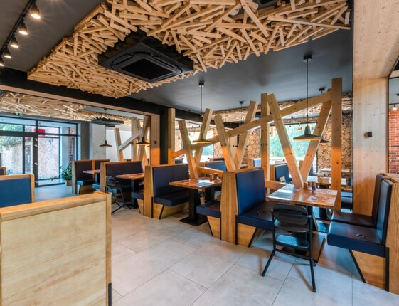 Contemporary hotel restaurant with wooden booths, navy upholstered seating, sculptural wood ceiling and pendant lights.
