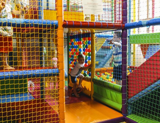 Indoor children's play area with colorful climbing frames, ball pit and safety nets, kids playing and exploring.