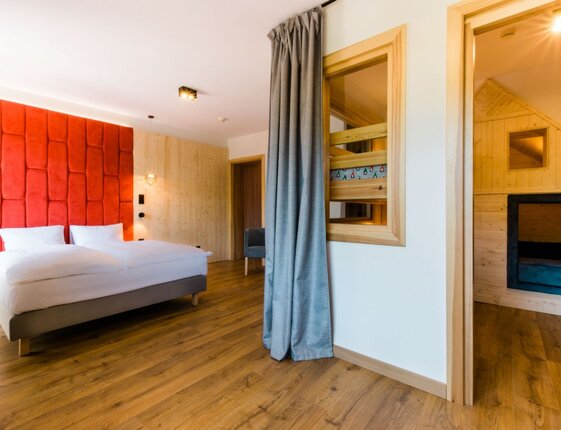 Spacious family suite with king bed, bold red upholstered headboard, wooden floors and a cozy children's alcove.