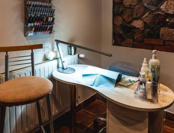 Cozy hotel manicure station: curved wooden table, LED task lamp, wall rack of nail polishes and manicure tools.