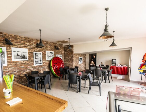 Hotel snack bar and lounge with wicker tables, exposed brick, drink fridge, life jackets and pool floats.